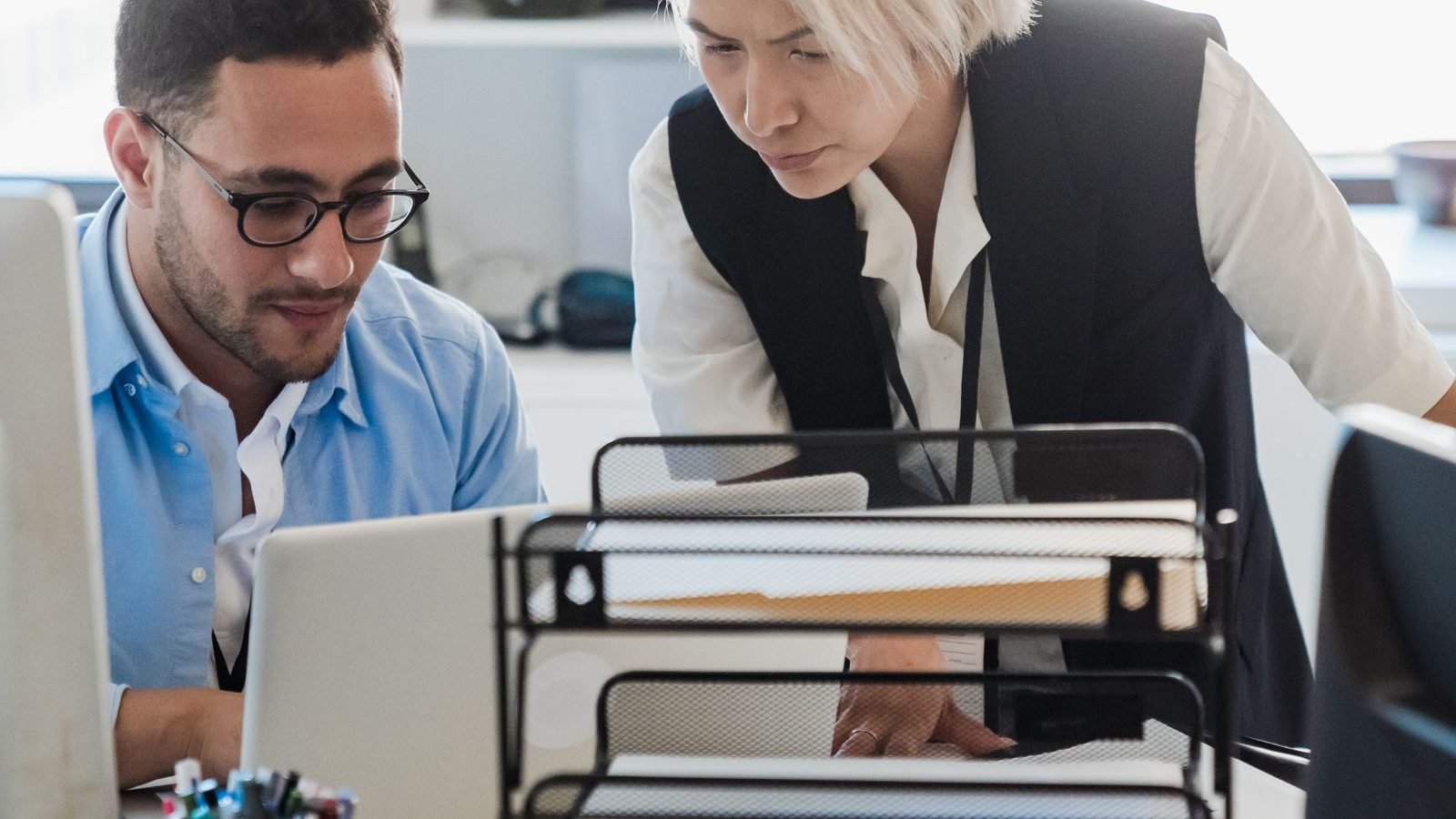 Two colleagues collaborating over a laptop in a bright, modern open-plan office.