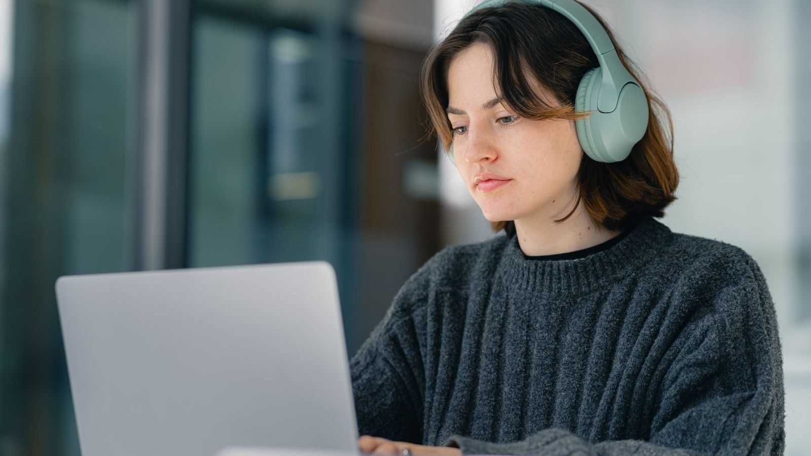 A focused individual wearing headphones, concentrating while working on a laptop in a quiet workspace.