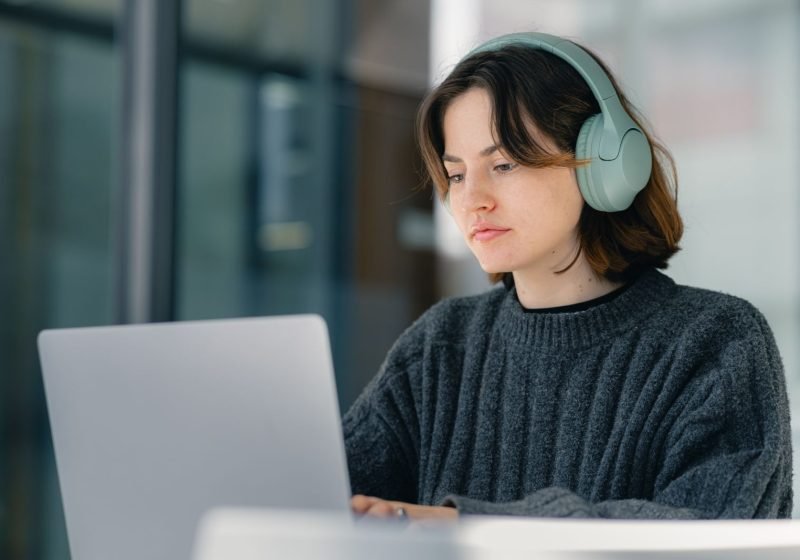 A focused individual wearing headphones, concentrating while working on a laptop in a quiet workspace.