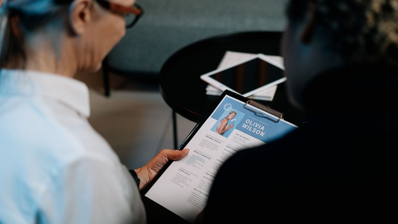 A professional reviewing a questionnaire on a clipboard with a new starter in an office setting.