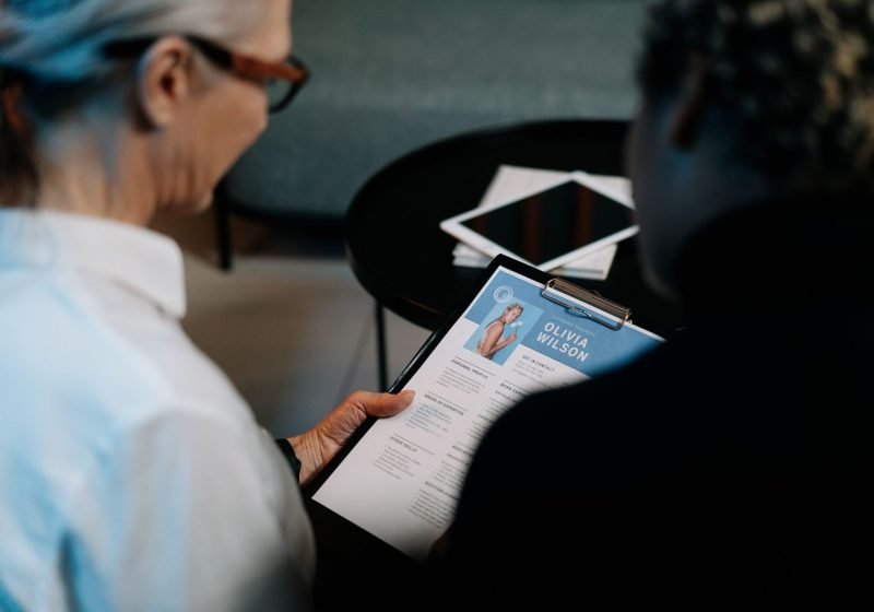 A professional reviewing a questionnaire on a clipboard with a new starter in an office setting.