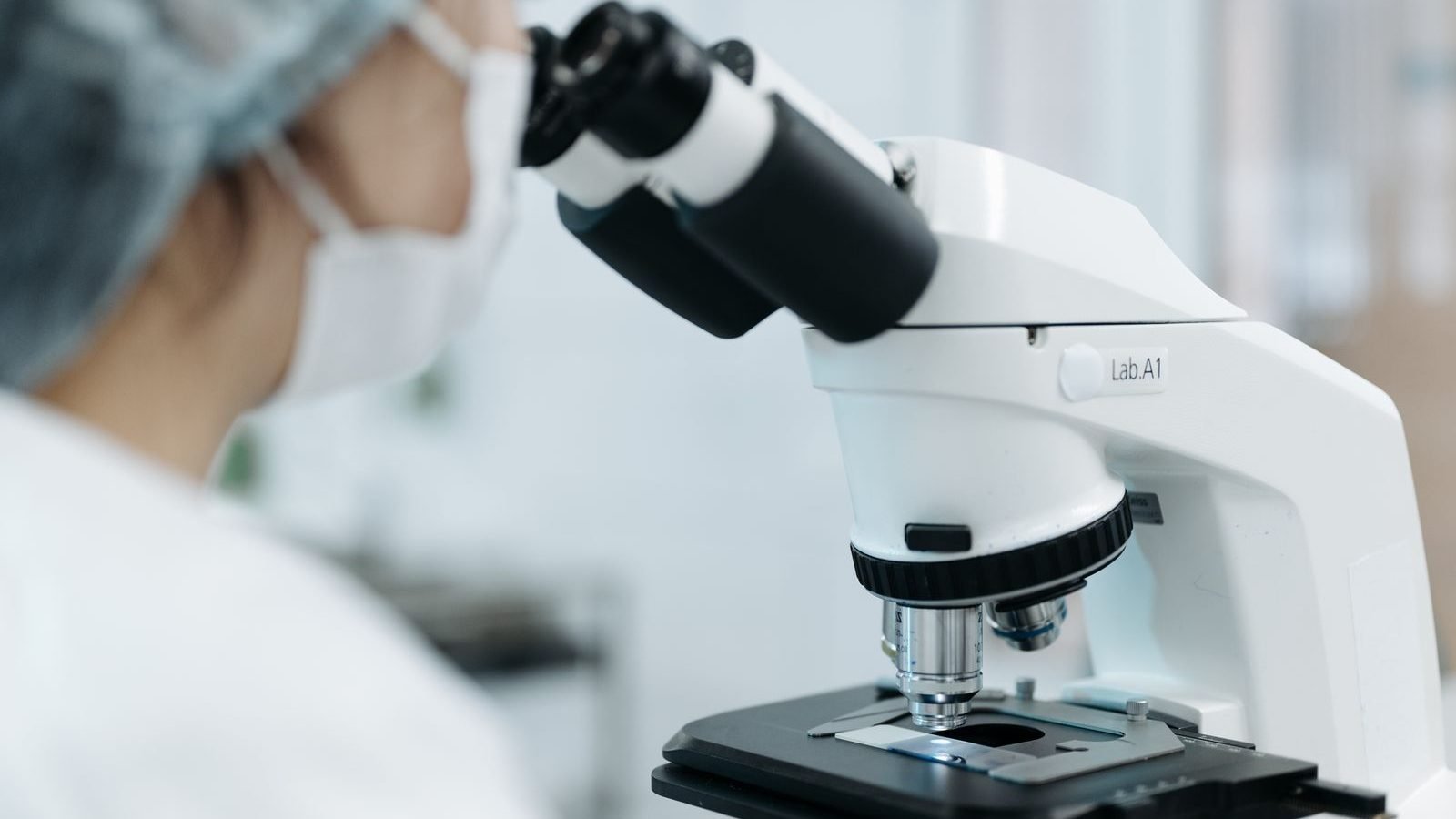 A clinician using a microscope to analyse samples in a clinical laboratory testing setting.