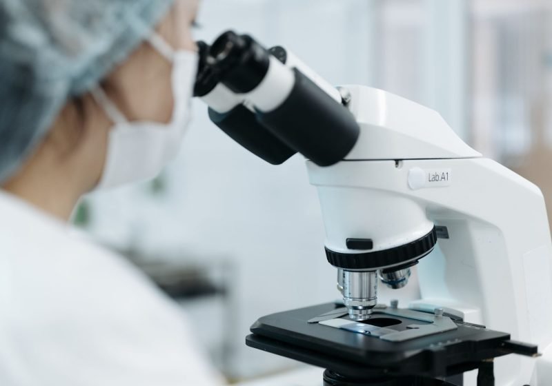 A clinician using a microscope to analyse samples in a clinical laboratory testing setting.