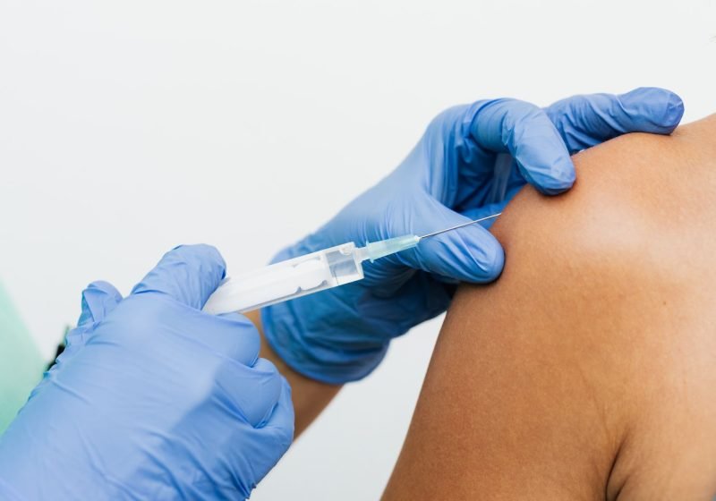 A nurse administering a vaccination into a person's upper arm at a workplace clinic.